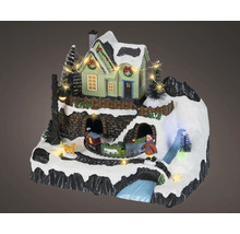 Kerstminiatuurdorp met verlicht huis, rijdende trein, kind, hond en besneeuwd berglandschap.