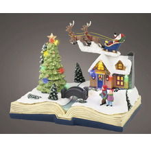 Miniatuur kersttafereel op een open boek met besneeuwd huis, kinderen, brug, verlichte kerstboom en vliegende kerstman.
