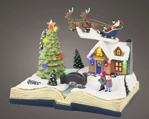 Miniatuur kersttafereel op een open boek met besneeuwd huis, kinderen, brug, verlichte kerstboom en vliegende kerstman.