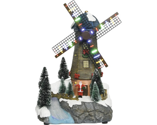 Kerstdecoratie met verlichte windmolen, kerstmanfiguur, besneeuwde dennenbomen en een beekje op een rotsachtige basis.