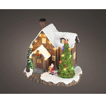 Miniatuur kersthuisje van hout met besneeuwd dak, verlichte kerstboom en klein kerstmanfiguurtje.