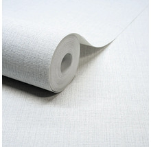 Lichtgrijs vliesbehang met een fijne linnenstructuur, een gedeeltelijk afgerolde rol behang.