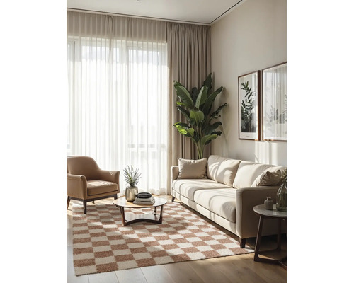 Moderne, lichte woonkamer met lichte bank, bruine fauteuil, geblokt vloerkleed, gordijnen en grote kamerplant.