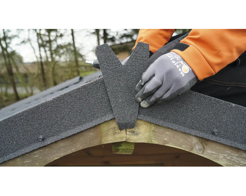 Montage van bitumen dakbedekking op de nok van een houten tuinhuis.