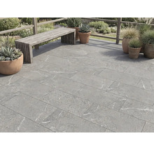 Terrastegels in steenlook met grijze marmering op een terras met houten bank en plantenpotten buiten.