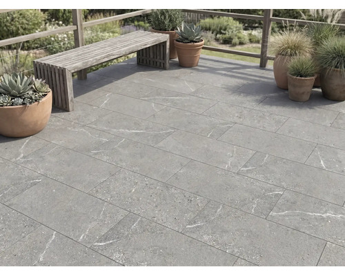 Terrastegels in steenlook met grijze marmering op een terras met houten bank en plantenpotten buiten.