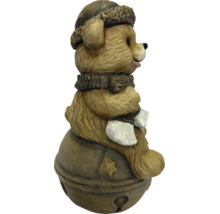 Decoratieve bruine beer met wintermuts en sjaal zittend op een bel met sterrenmotief.