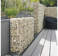 Schanskorf wand gevuld met lichte stenen op een terras met grijze vlonderplanken en een schutting in de tuin.