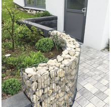 Gebogen schanskorf als tuinborder, gevuld met lichte natuurstenen naast een bestraat pad.
