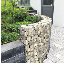 Gebogen schanskorf van gaas gevuld met natuursteen als border voor een tuinperk naast een bestraat pad.