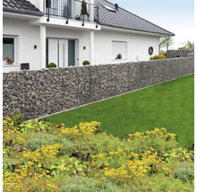Lange schanskorf wand van natuursteen in een lichte tuin met gazon voor een woonhuis met balkon.
