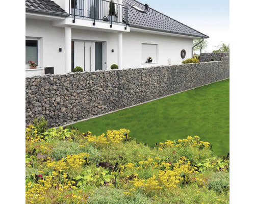 Lange schanskorf wand van natuursteen in een lichte tuin met gazon voor een woonhuis met balkon.