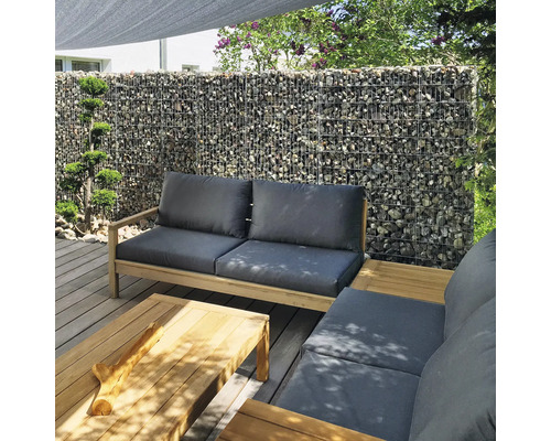 Moderne tuinlounge op houten terras met schanskorfwand op de achtergrond, houten meubels met grijze kussens en bijpassende salontafel.