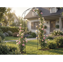 Zwarte metalen rozenboog met roze en witte klimrozen in een lichte, georganiseerde tuin voor een woonhuis.