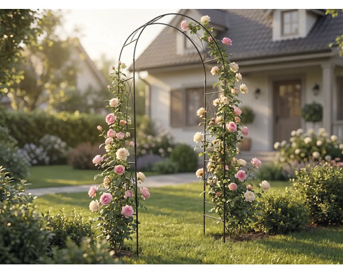 Zwarte metalen rozenboog met roze en witte klimrozen in een lichte, georganiseerde tuin voor een woonhuis.