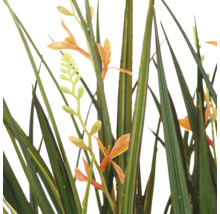 Detailopname van een kunstplant met lange groene grassprieten en kleine oranje bloemen.