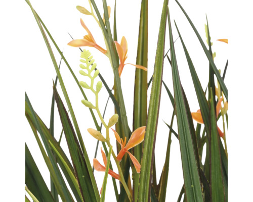 Detailopname van een kunstplant met lange groene grassprieten en kleine oranje bloemen.
