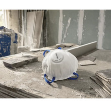 Wit Rautner stofmasker met uitblaasventiel en blauwe hoofdbanden op een stoffige bouwplaats.