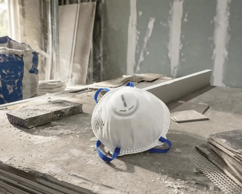 Wit Rautner stofmasker met uitblaasventiel en blauwe hoofdbanden op een stoffige bouwplaats.