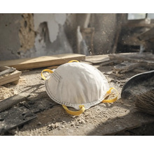 Wit stofmasker op een stoffige werkbank in een werkplaats met gereedschap, houtresten en zaagsel.