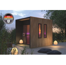 Moderne Karibu tuinsauna met houten lamellengevel en twee ramen, geplaatst op een houten terras met buitenverlichting en zitkussens.