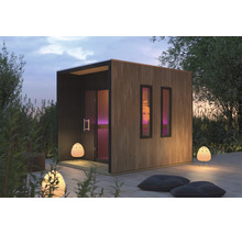 Moderne tuinsauna met verticale houten lattengevel en twee smalle ramen op een houten terras in de tuin.