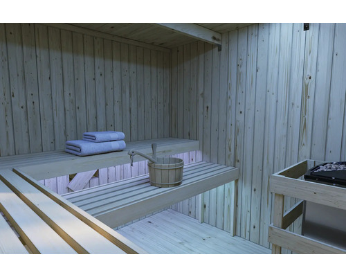 Binnenaanzicht van een moderne houten sauna met getrapte saunabanken, sauna-emmer en handdoeken en een saunakachel.
