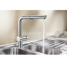 Moderne metalen keukenkraan met één hendel, uittrekbare handdouche en stromend water boven een roestvrijstalen spoelbak.
