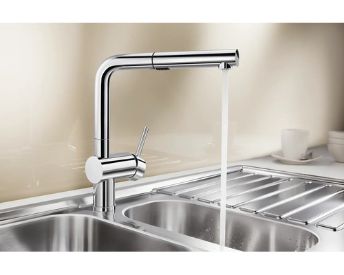 Moderne metalen keukenkraan met één hendel, uittrekbare handdouche en stromend water boven een roestvrijstalen spoelbak.