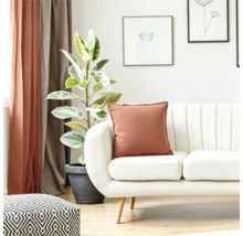 Een lichte woonkamer met een witte bank, een decoratief kussen in roestbruin, een kamerplant in een pot en een poef met geometrisch patroon.