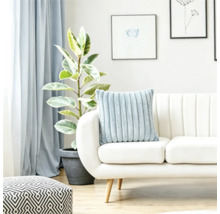Een zacht geribbeld kussen op een lichte bank in een lichte woonkamer met een plant en een geometrische poef.
