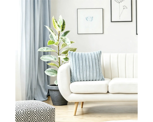 Een zacht geribbeld kussen op een lichte bank in een lichte woonkamer met een plant en een geometrische poef.