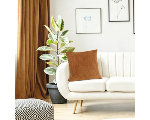Een sierkussen op een moderne witte bank in de woonkamer met een kamerplant en gordijnen op de achtergrond.