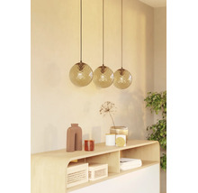 Drie hangende kogelvormige lampen met een gestructureerd oppervlak boven een houten dressoir met decoratieve items.