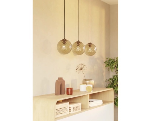 Drie hangende kogelvormige lampen met een gestructureerd oppervlak boven een houten dressoir met decoratieve items.