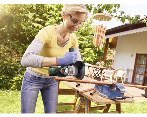 Vrouw werkt in de tuin met een haakse slijper aan een koperen buis die in een bankschroef is bevestigd