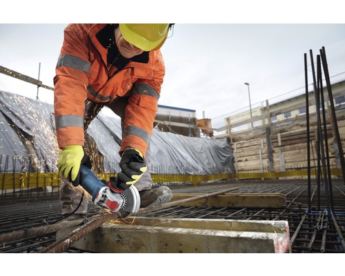 Een bouwvakker snijdt met een haakse slijper stalen staven op een bouwplaats.