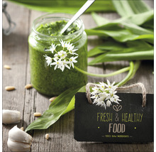 Weckpot met daslookpesto, daslookbladeren, teentjes knoflook en een bord met de tekst verse en gezonde voeding op een houten tafel