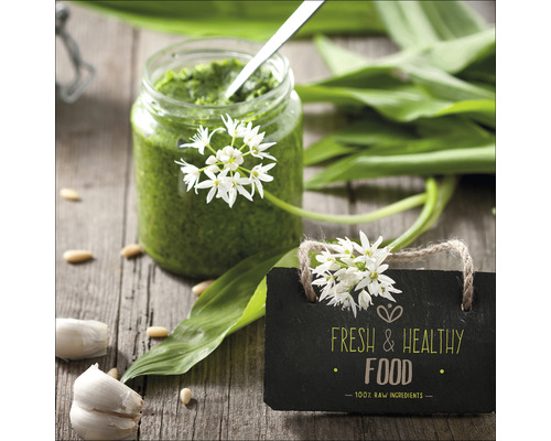 Weckpot met daslookpesto, daslookbladeren, teentjes knoflook en een bord met de tekst verse en gezonde voeding op een houten tafel