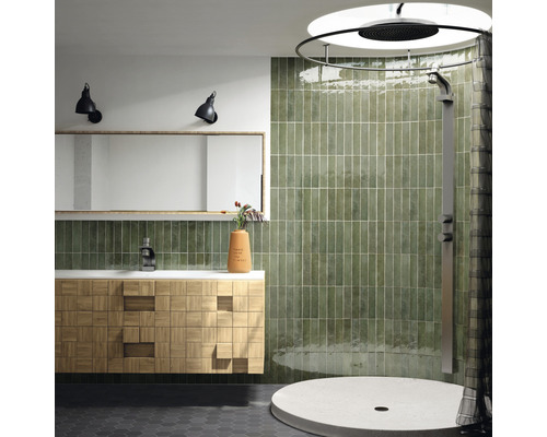 Badkamer met douche, wastafel, spiegel en groene tegels.