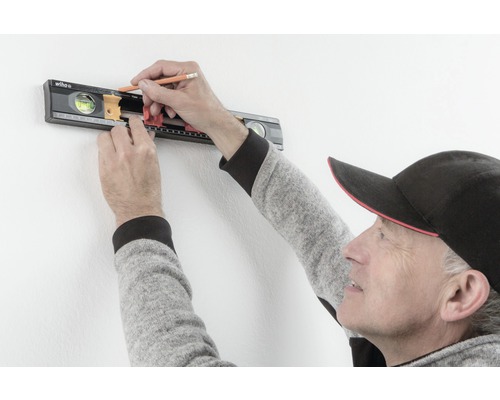 Een persoon gebruikt een waterpas van Wiha op een muur en markeert een plek met een potlood.