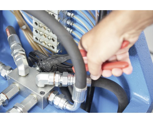 Hand die met een tang aan een hydraulische leiding werkt