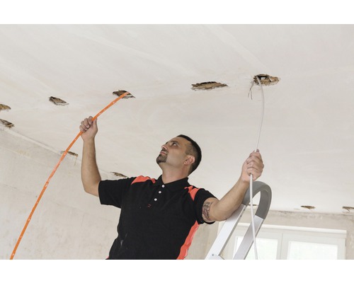 Elektricien trekt kabels in een plafond met installatieopeningen.