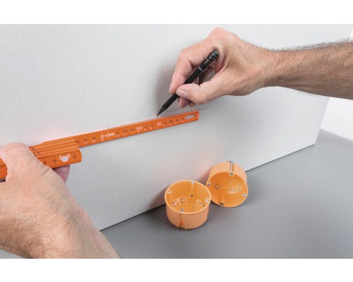 Hand tekent met potlood een lijn met een duimstok op een plaat, installatiedozen liggen klaar.