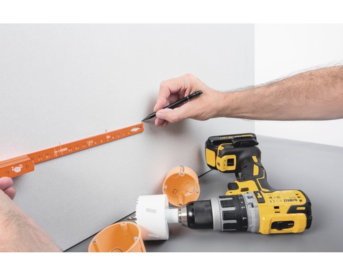 Een persoon markeert met een potlood en duimstok de positie voor een boring naast een boormachine en gatenzaag