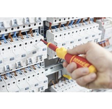 Een elektricien werkt met een geïsoleerde schroevendraaier aan een elektrische installatie.