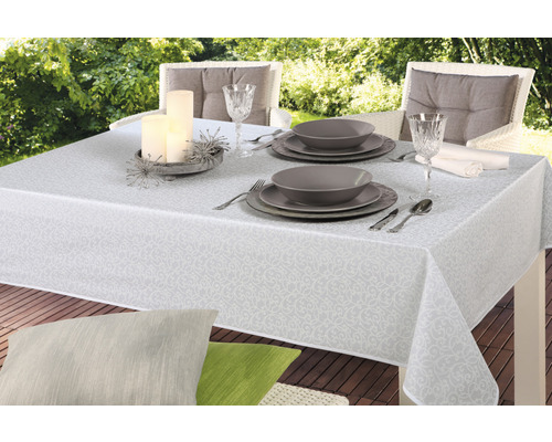 Gedekte tuintafel met wit tafelkleed met patroon, servies, glazen en kaarsen