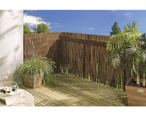 Terras met rieten privacyscherm, houten vloer en potplanten.