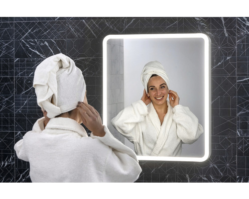 Vrouw met handdoek op het hoofd voor een verlichte badkamerspiegel