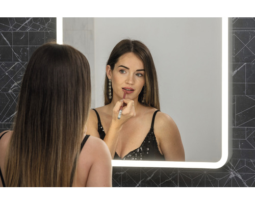 Vrouw brengt lippenstift aan voor een verlichte spiegel in de badkamer